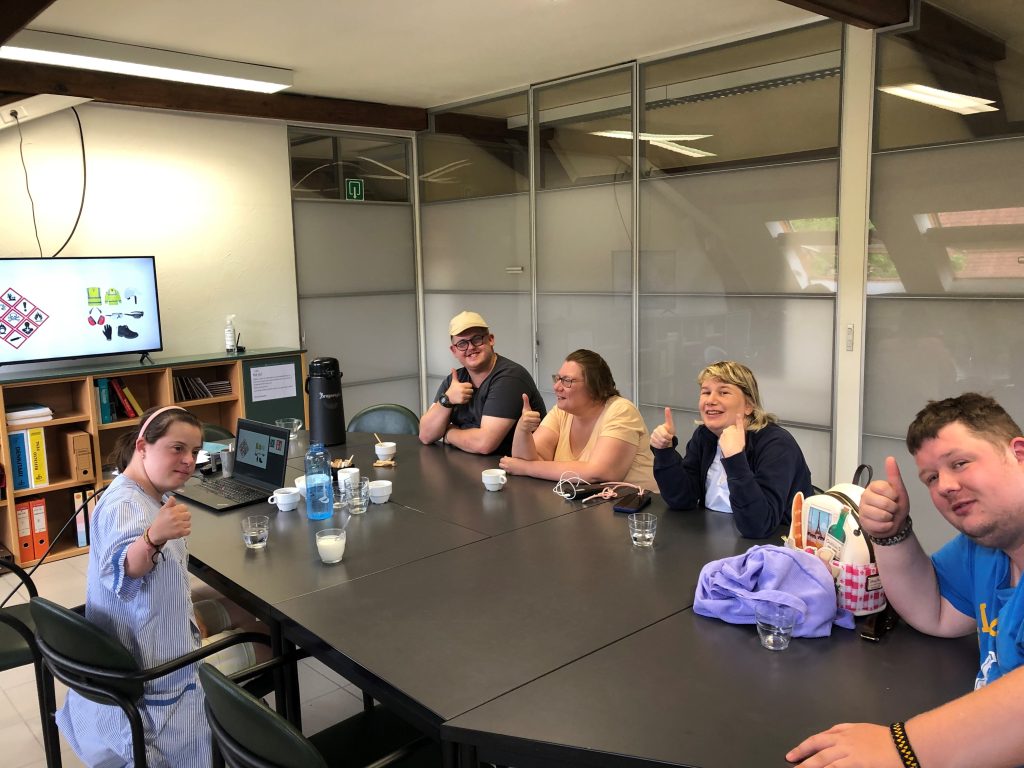 Ubuntu's meeting with people with disabilities. Two women and three men with intelectual disabilities are sitting around a black desk, posing for the picture.